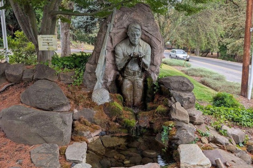 A statue of a man holding a shovel, surrounded by rocks and a small stream. 5
