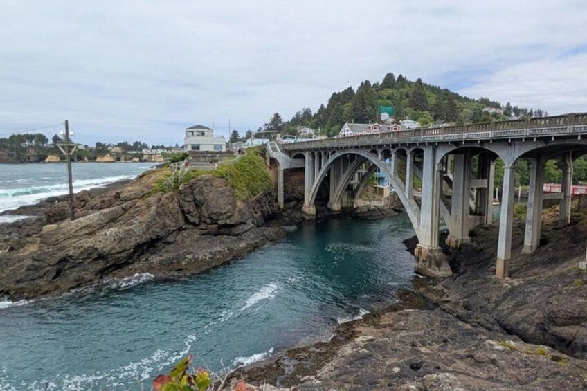 A coastal bridge, rocky shoreline, and a hill with buildings in the background. 2