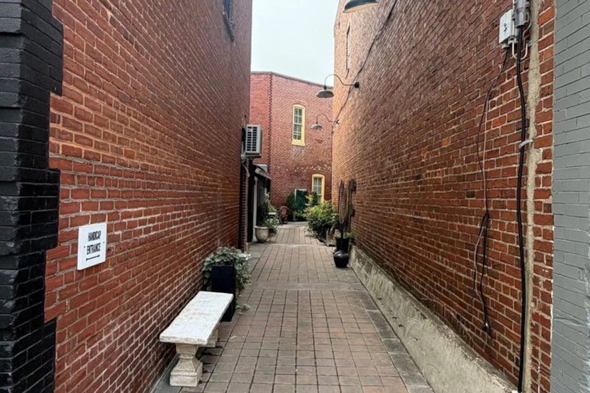 A narrow alleyway with brick walls, a bench, and a sign indicating a no parking zone. 5