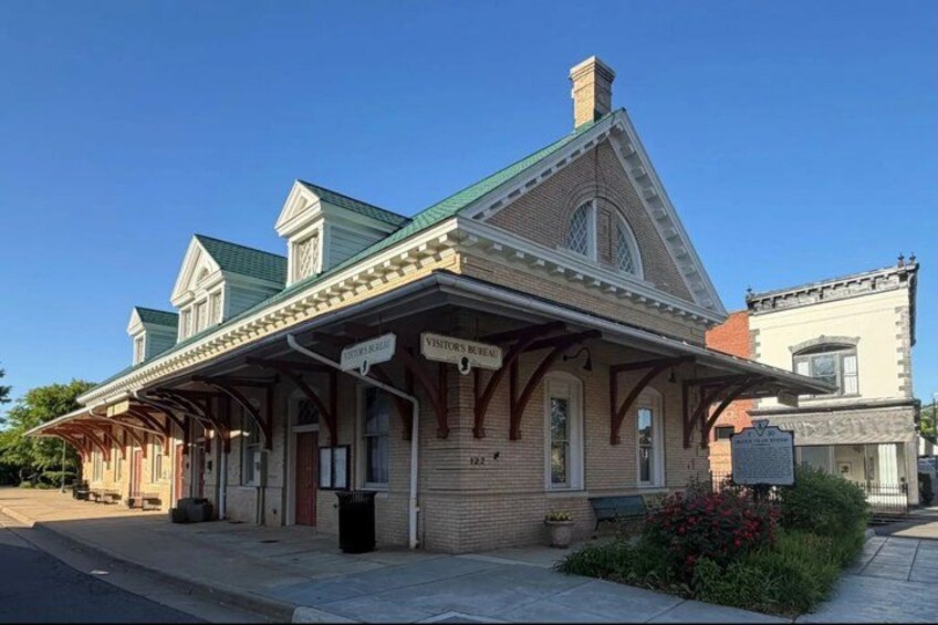 A historic train station with a covered waiting area, a clock, and a sign indicating the station's name. 2