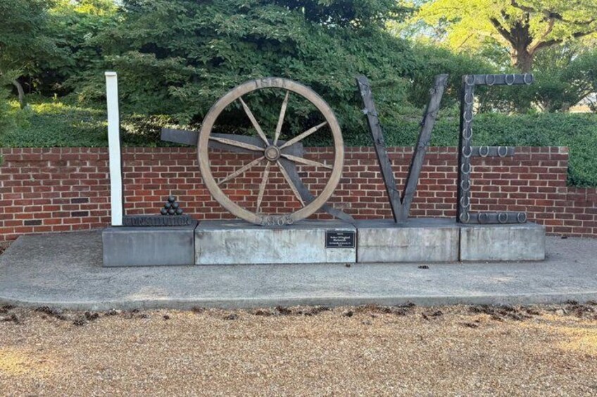 A metal sculpture with a large wheel and letters spelling 'LOVE' against a brick wall. 3