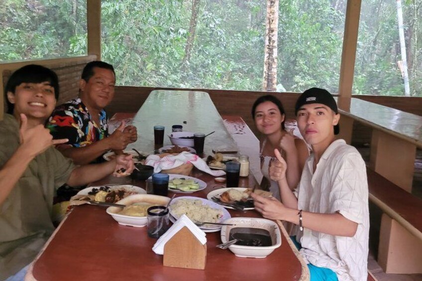 A group of people dining at a wooden table with various dishes and a small house-shaped container. 1