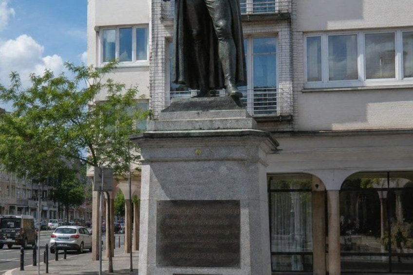 A statue on a pedestal in an urban setting with buildings and trees in the background. 2