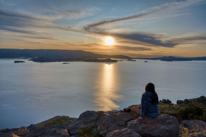 A person sitting on a rock overlooking a calm body of water with a sunset in the background. 4