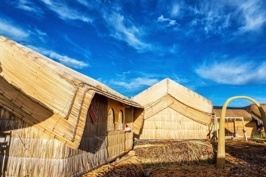 Traditional wooden structures with thatched roofs, set against a clear blue sky. 1