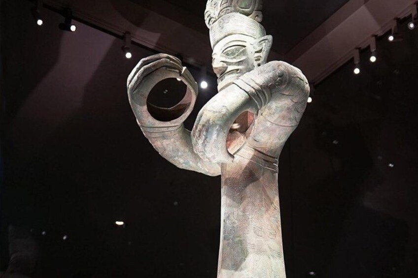 A large, ancient bronze statue with intricate carvings and a circular opening on its chest. 3