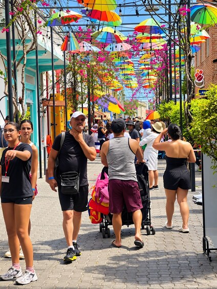 A street lined with colorful umbrellas, people walking, and buildings with blue and white facades. 5