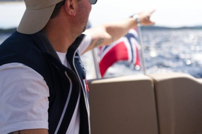 Een persoon in een wit shirt en donker vest wijst richting het water. 5