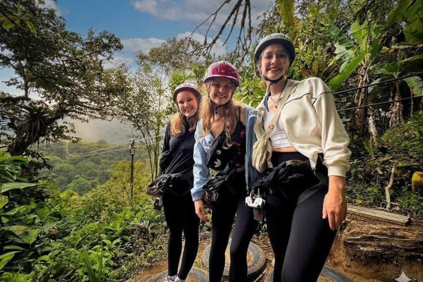 Three people wearing helmets and backpacks, standing on a trail with lush greenery and a view of a valley. 3