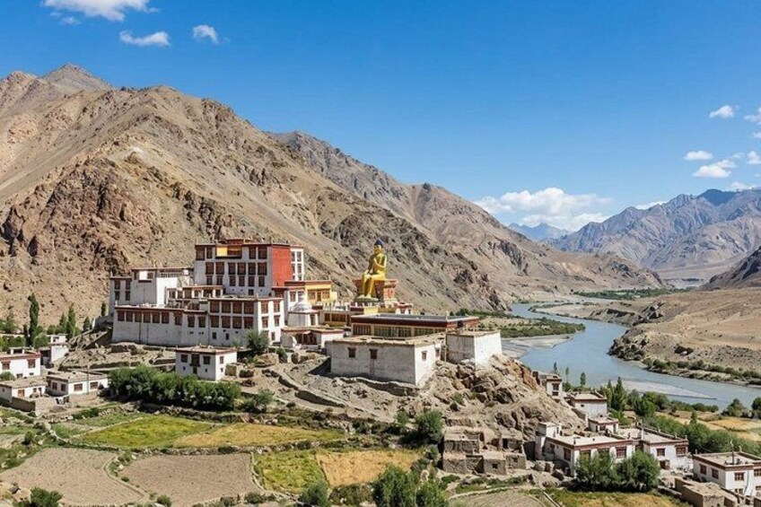 A monastery complex with a large golden statue, surrounded by mountains and a river. 1