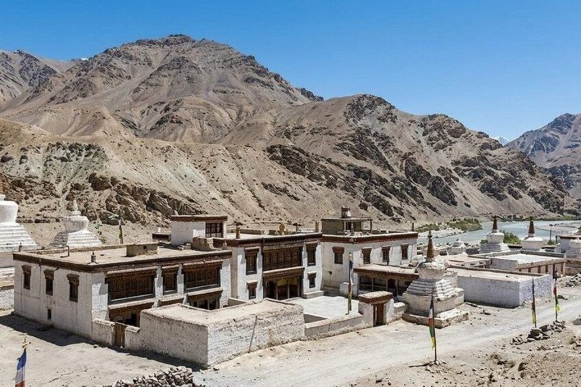 A mountainous landscape with a monastery complex, including buildings and prayer wheels. 3