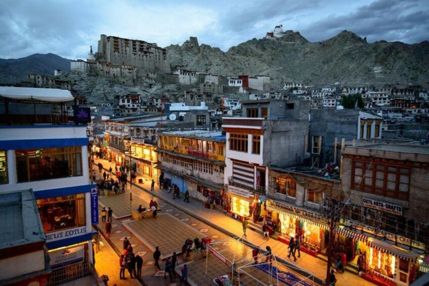 A bustling street with shops and a historic fortress in the background. 2