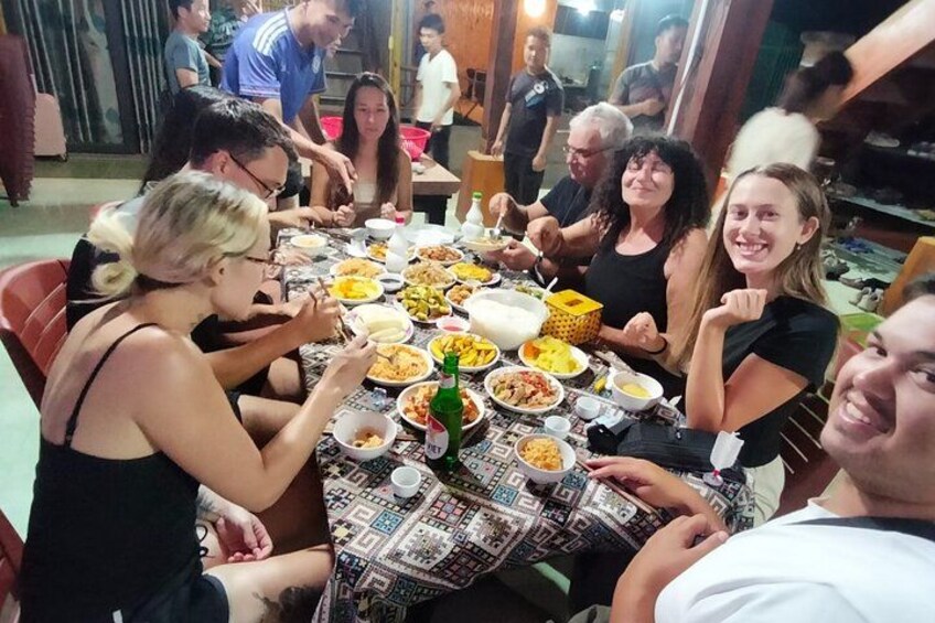 Un grupo de personas sentadas alrededor de una mesa con varios platos y una botella de cerveza. 3