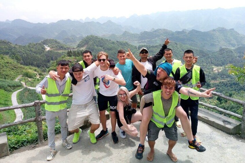 Un grupo de personas en un sendero de montaña con una vista panorámica de colinas verdes y una carretera serpenteante al fondo. 1