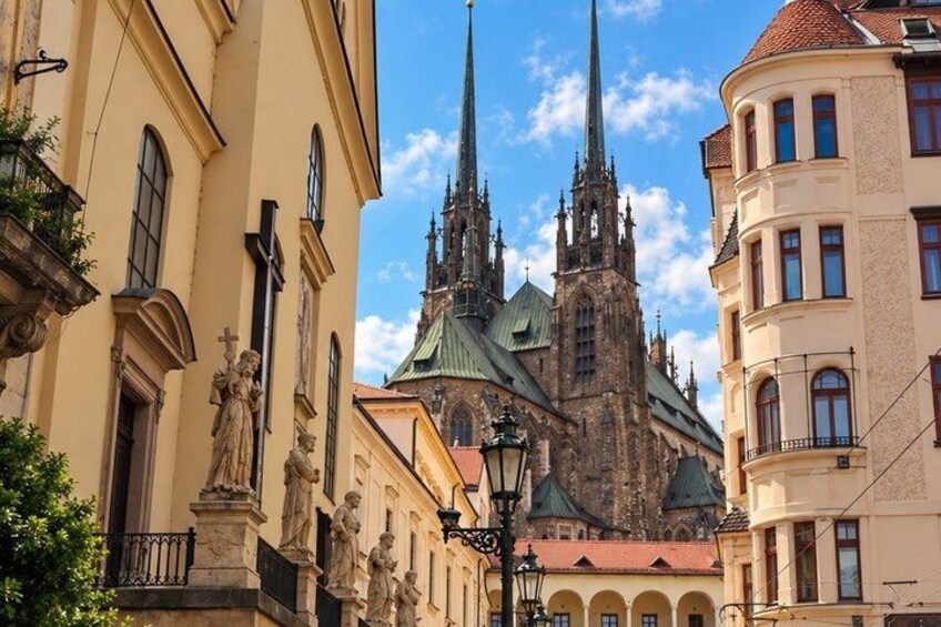 A historic church with a tall spire, a statue of a woman, and a building with a balcony. 4