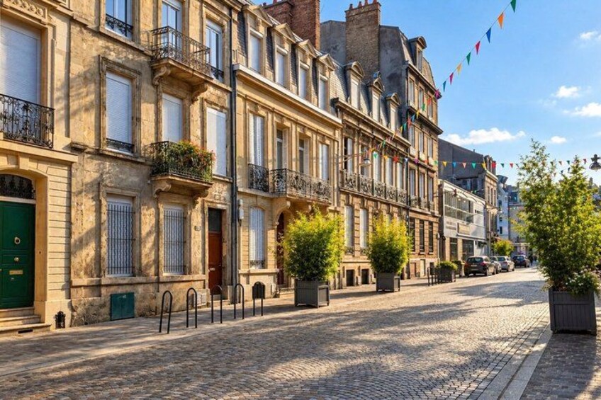 A cobblestone street lined with historic buildings, a clear sky, and a few cars parked along the road. 3