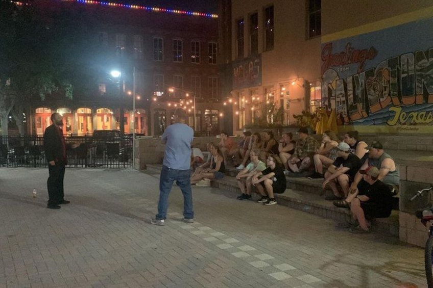 A group of people sitting on steps at night, a street with lights, and a building with a sign. 4