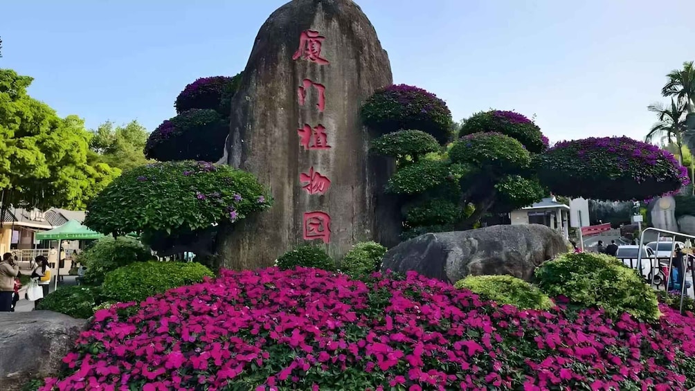 A large stone monument with Chinese characters, surrounded by lush greenery and vibrant pink flowers. 3