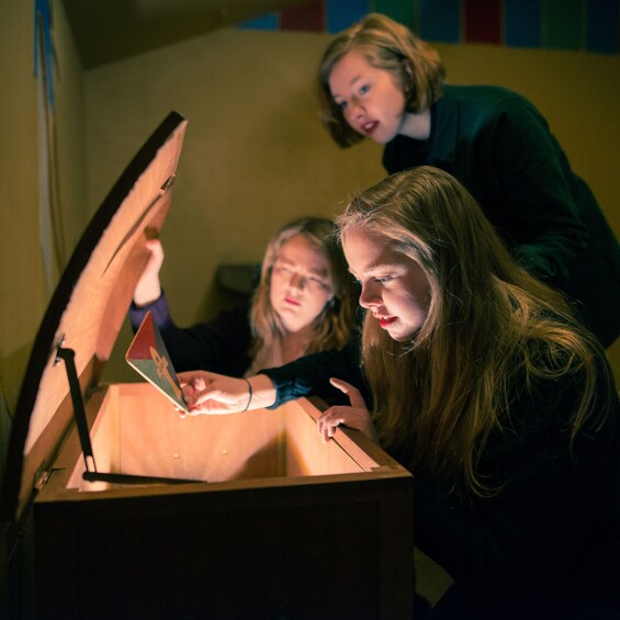 Three individuals engaged with a laptop inside a wooden box. 3