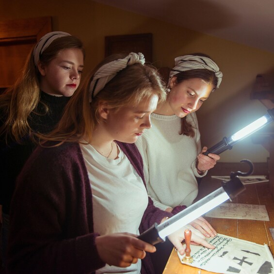 Three individuals examining a document with a flashlight. 4