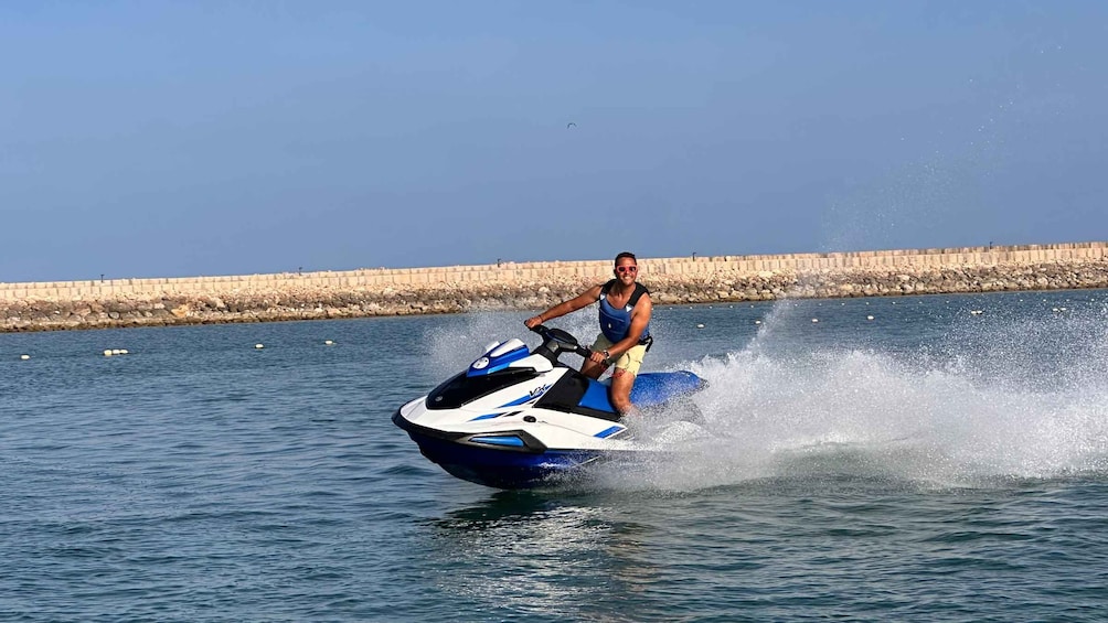 A person riding a jet ski on water with a rocky breakwater in the background. 1