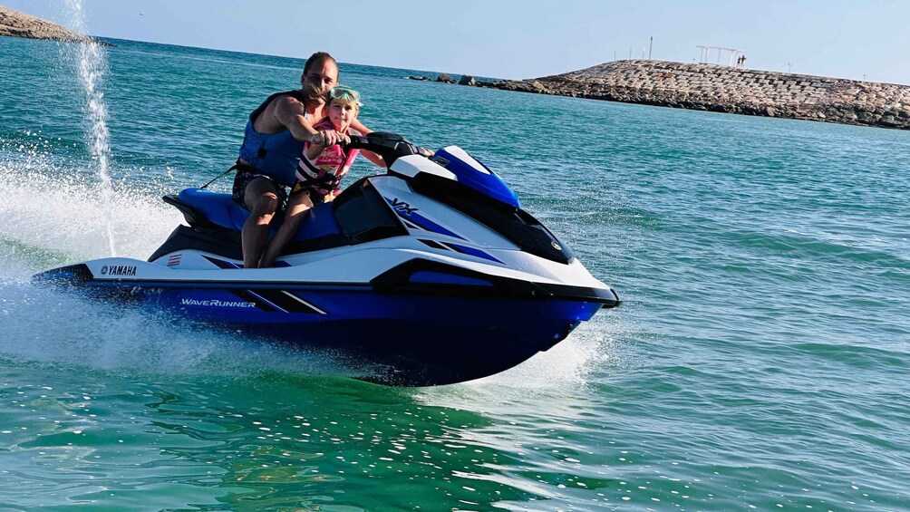 A person riding a Yamaha WaveRunner jet ski on turquoise water with a rocky breakwater in the background. 3