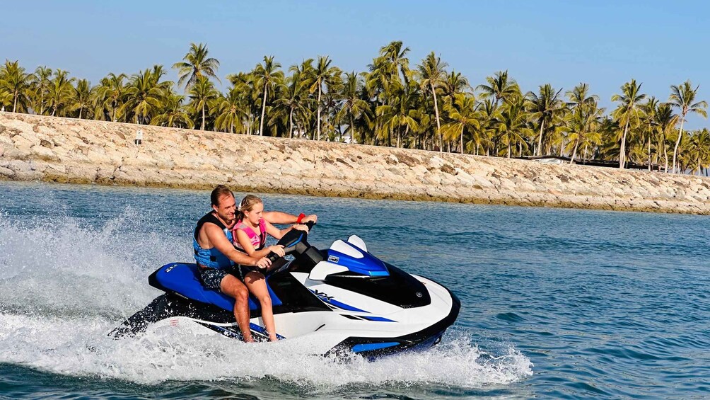 A person jet-skiing on a body of water with a rocky shoreline and palm trees in the background. 2
