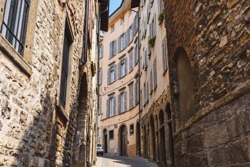 A narrow street flanked by historic stone buildings with arched doorways and windows. 5