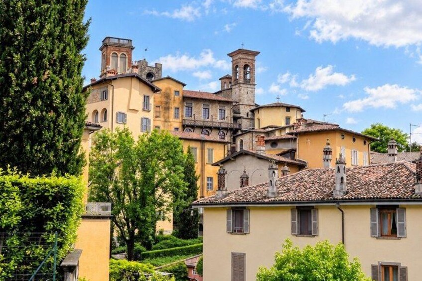 A historic town with terracotta-roofed buildings, a prominent bell tower, and lush greenery. 2