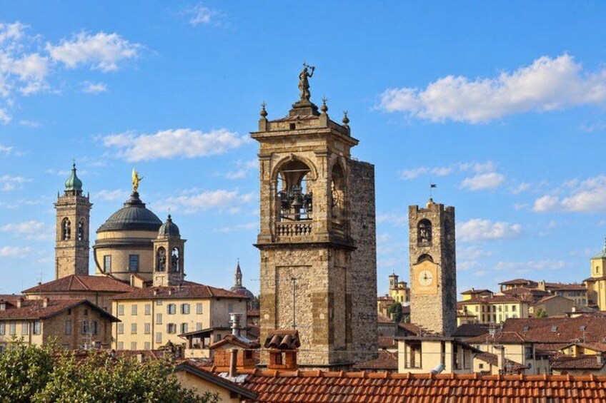 A historic cityscape with a prominent bell tower, domed buildings, and a clear blue sky. 3