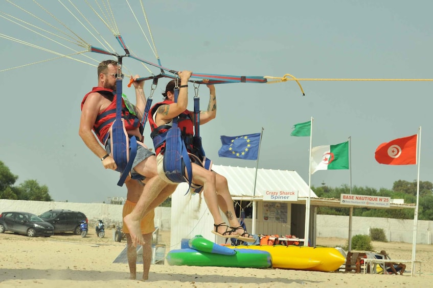Twee personen bezig met parasailen, met vlaggen en een bord waarop een nautische basis wordt aangegeven op de achtergrond. 4