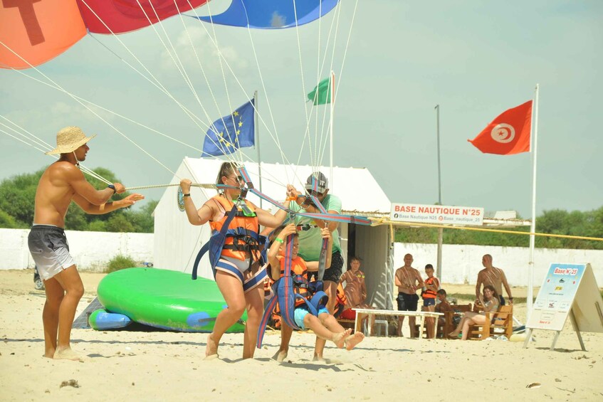 Een strand met mensen die een touwtrekwedstrijd houden, ze dragen reddingsvesten en tuigjes. 2