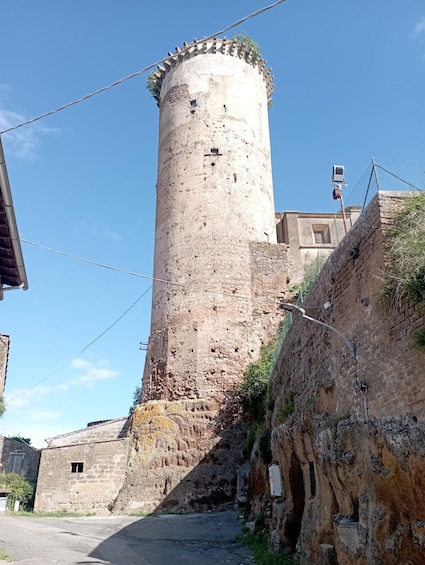 A historic stone tower with a crenellated top, surrounded by a stone wall and a paved road. 5