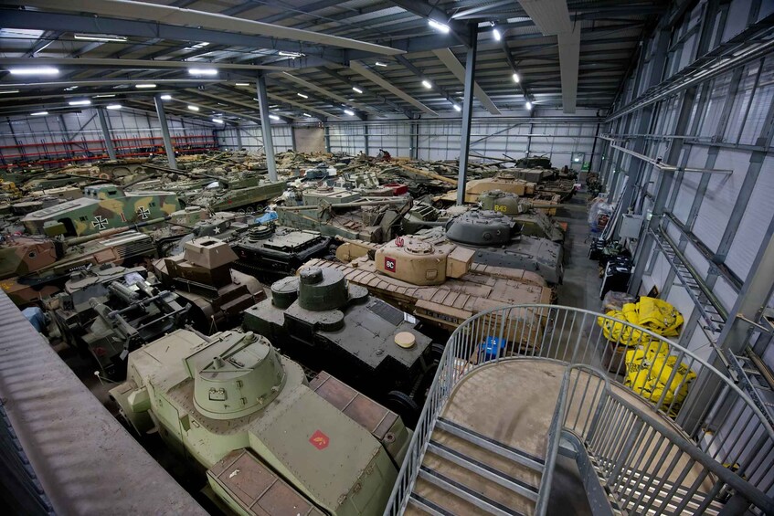 A large indoor storage area with numerous military vehicles, including tanks and armored vehicles, arranged in rows. 4