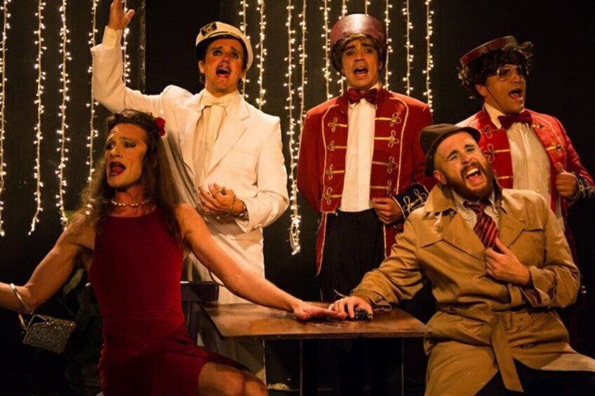 A group of people in theatrical costumes on a stage with string lights in the background. 1