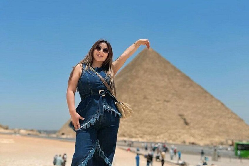 A person in a blue outfit standing in front of the Great Pyramid of Giza. 4