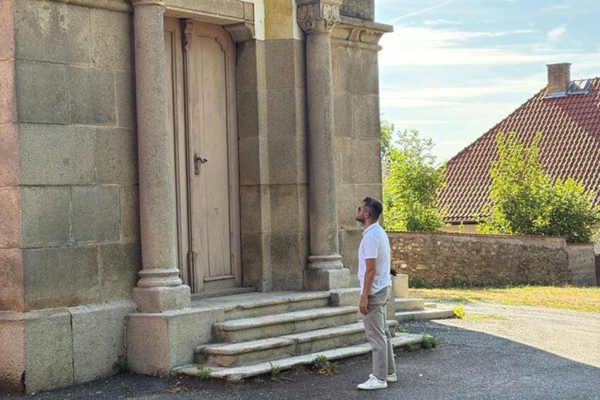 A man standing on steps in front of a building with a large wooden door. 3