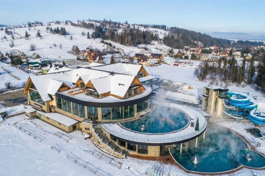 A large resort with a circular pool, wooden cabins, and a snowy landscape. 2