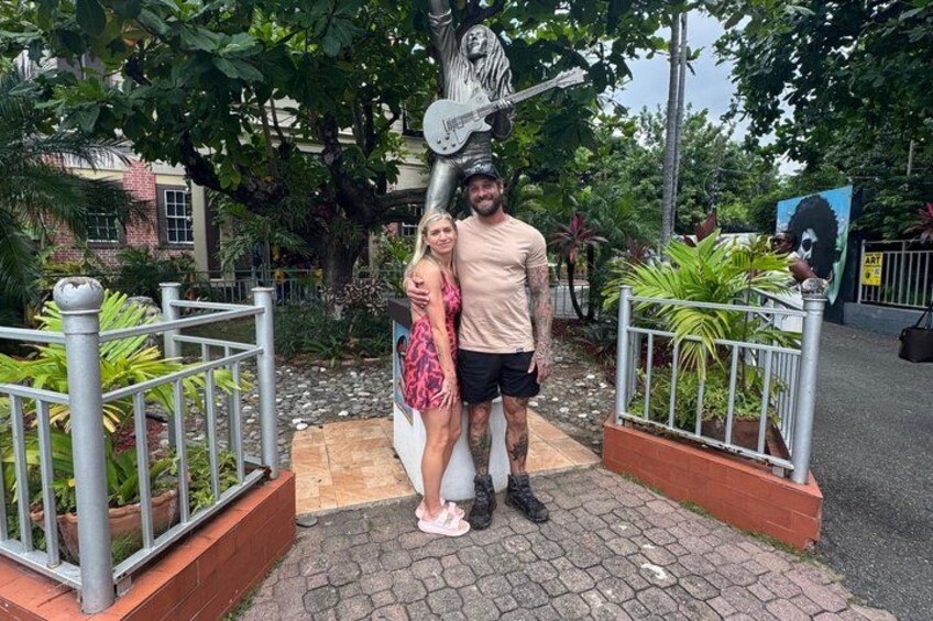 A man and a woman posing in front of a statue with a guitar. 1