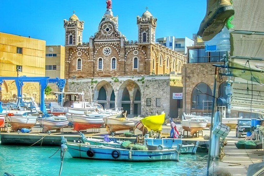 A harbor with boats docked in front of a historic building with arches and a bell tower. 3