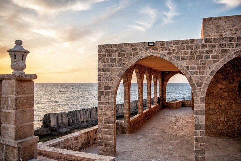 A stone walkway with arches leading to the sea, a stone railing, and a lamp post. 2