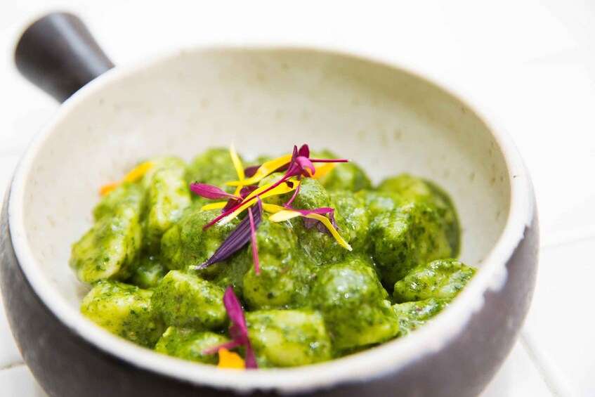 A bowl of green food garnished with purple and yellow flowers. 1