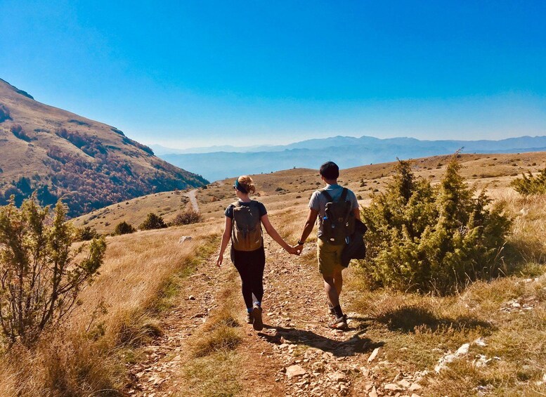 Dos personas caminando por un sendero rocoso, con un paisaje montañoso al fondo. 1