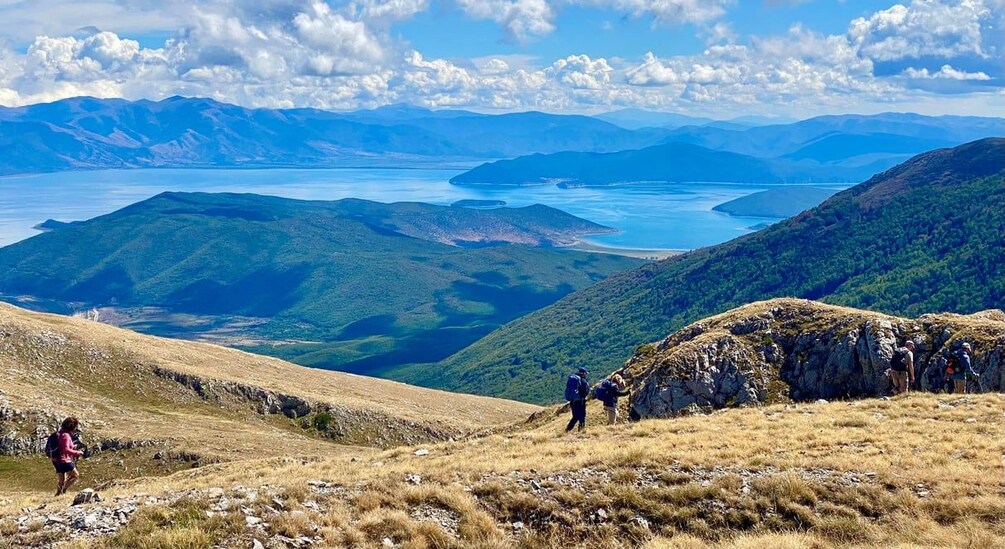 Senderistas en un sendero de montaña con un lago y montañas al fondo. 3