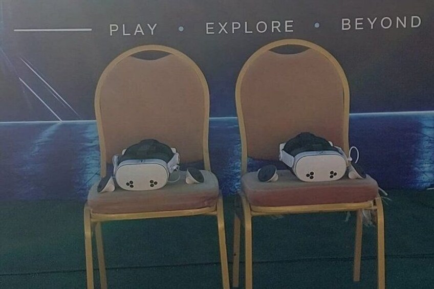 Two VR headsets on chairs with a backdrop featuring the words 'PLAY • EXPLORE • BEYOND'. 1
