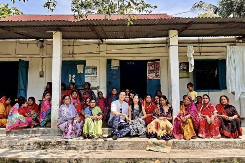 A group of people sitting on steps in front of a building with a corrugated metal roof. 1