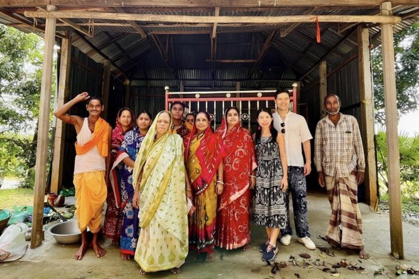 A group of people standing under a wooden shelter with a metal roof, surrounded by greenery. 3