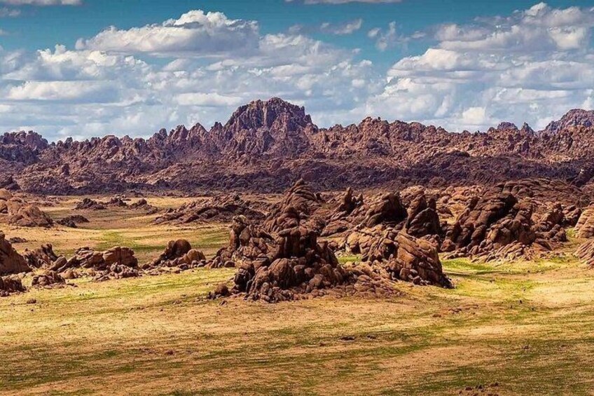 A rugged landscape with rocky formations and a distant mountain range under a partly cloudy sky. 2