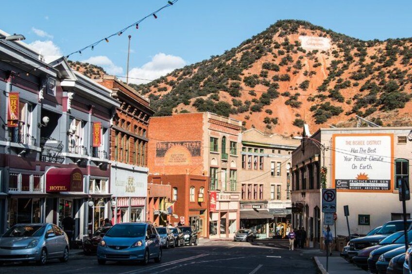 A street lined with historic buildings, a mountain in the background, and a sign advertising a local attraction. 2