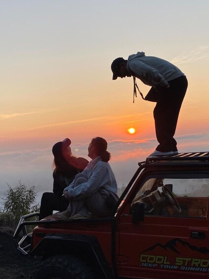 Tre personer sidder i et køretøj med solnedgang i baggrunden. 3